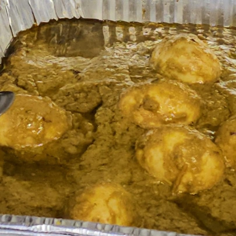 Close-up of golden-brown chicken pieces simmering in a rich, green curry sauce in a foil pan.