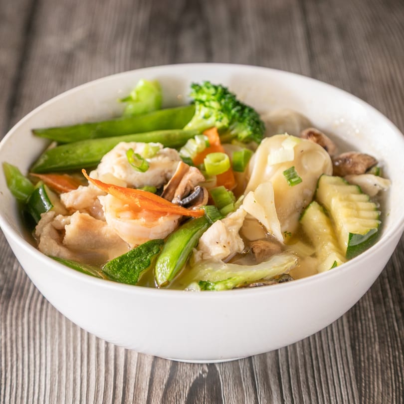 A white bowl of Vinsar's Lounge Asian-fusion soup with shrimp, chicken, dumplings, and vegetables.