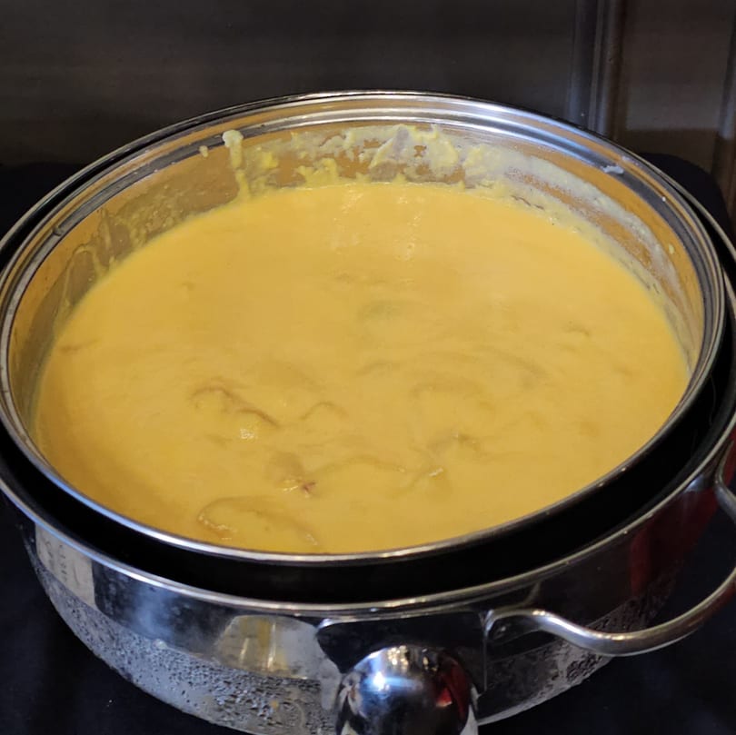 A large silver chafing dish filled with creamy yellow cheese sauce, ready for serving.