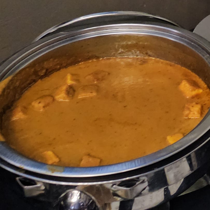 Paneer butter masala, a creamy orange Indian curry with paneer cubes, in a silver chafing dish.