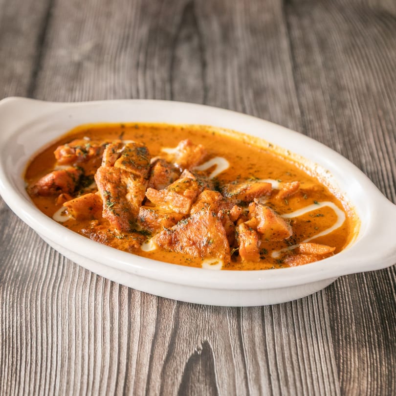 Vinsar's Lounge Asian-Indian fusion chicken curry in a white dish on a wooden table.