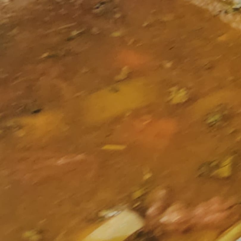 A close-up, blurry view of a brown stew with visible pieces of meat and vegetables.